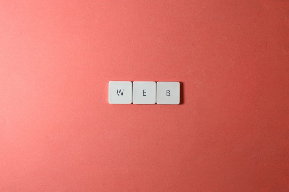 A close-up image displays three white rectangular tiles arranged horizontally on a solid pink background. Each tile features a single black letter, collectively spelling out the acronym 'WEB'. The sur